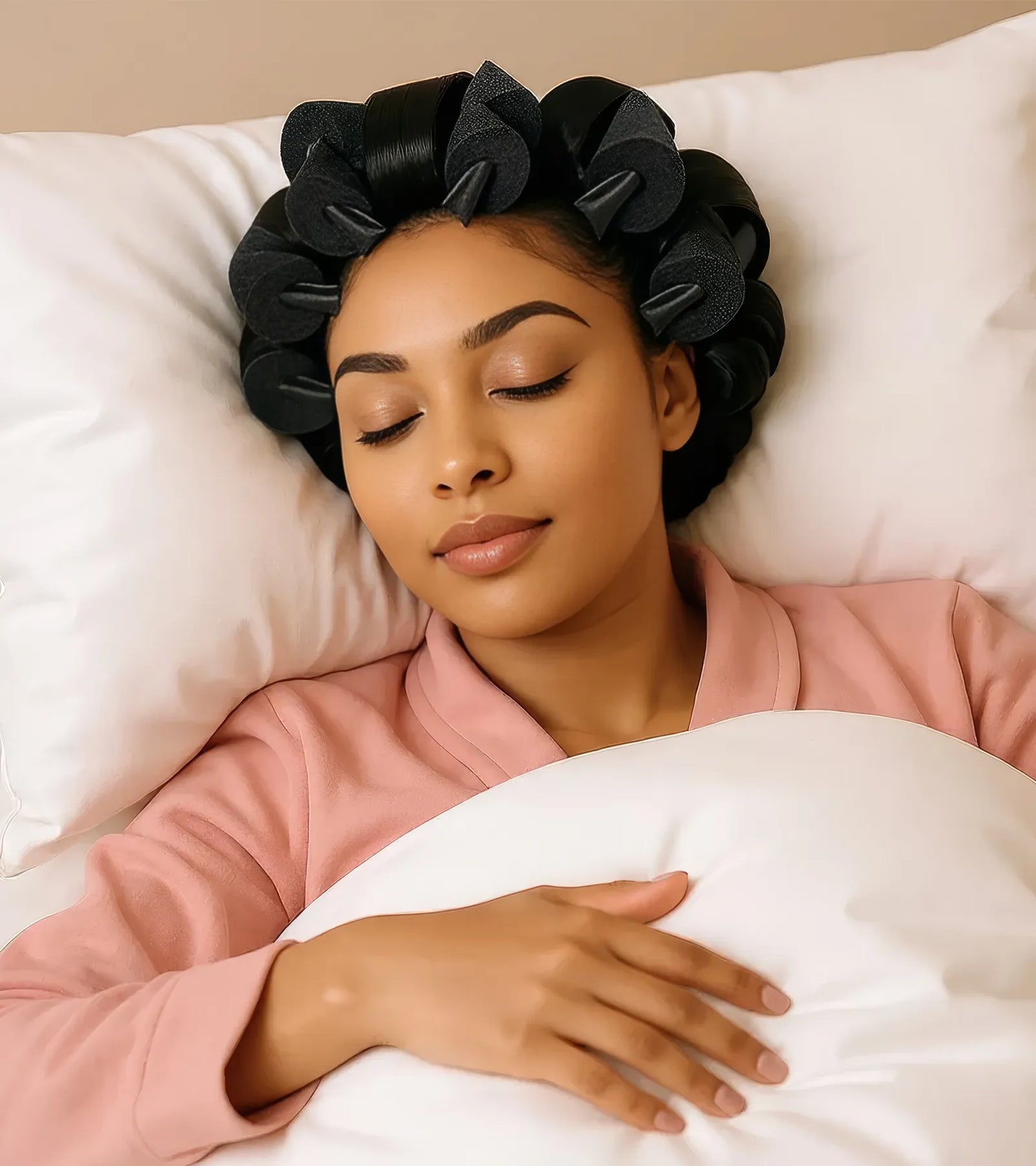 Woman lying in bed with hair rollers and pink pajamas, smiling.